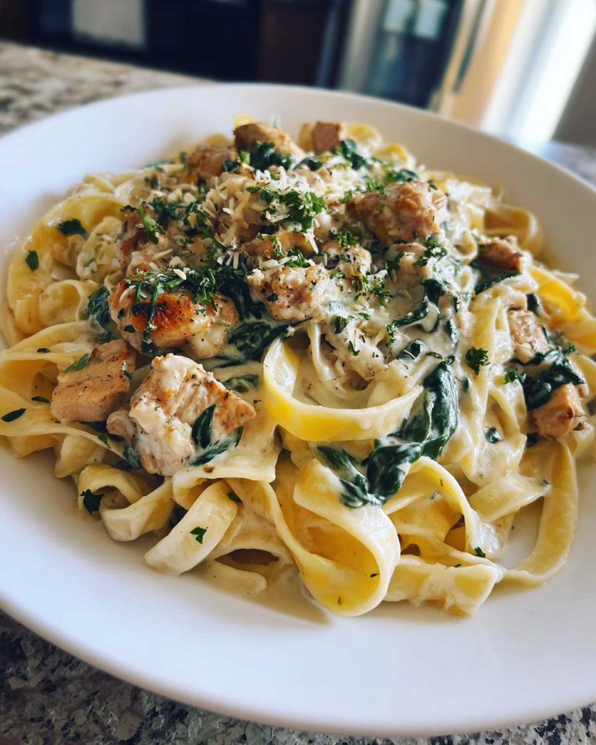 A close-up of a white bowl filled with Creamy Spinach Alfredo Pasta with Chicken, topped with Parmesan.
