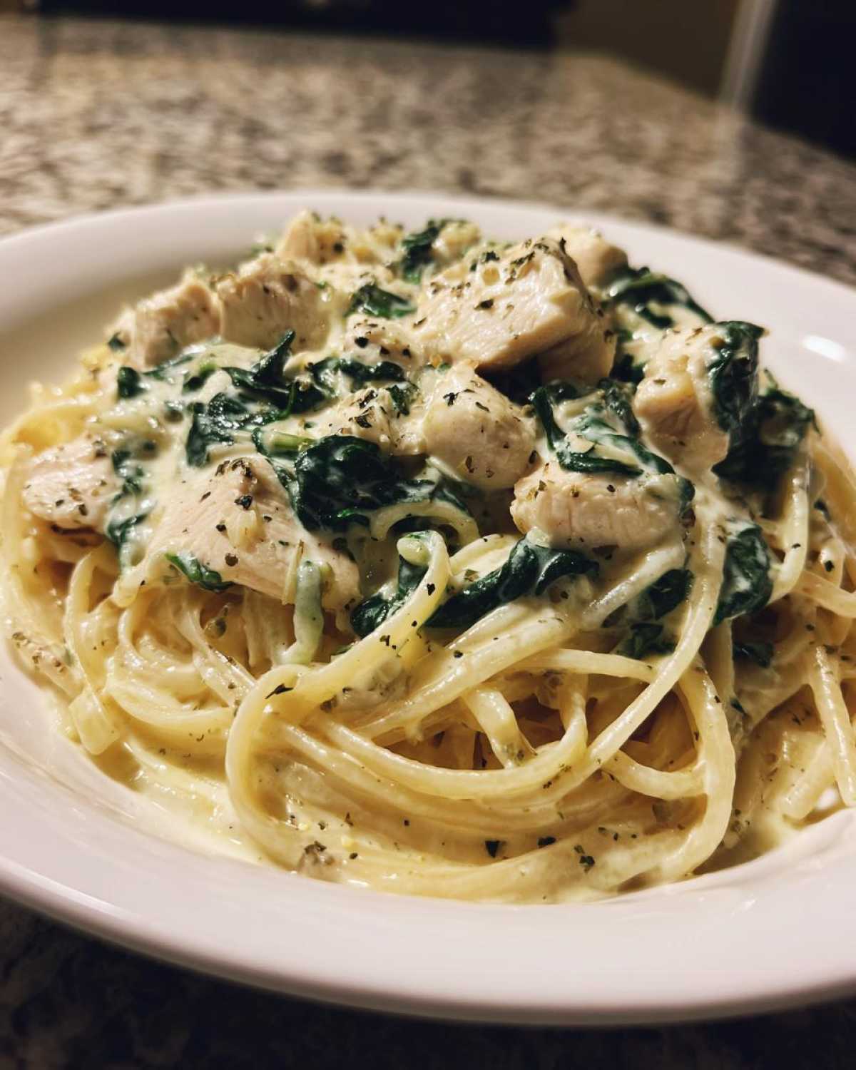 A close-up of Creamy Spinach Chicken Pasta with Alfredo Sauce, topped with diced chicken and herbs.