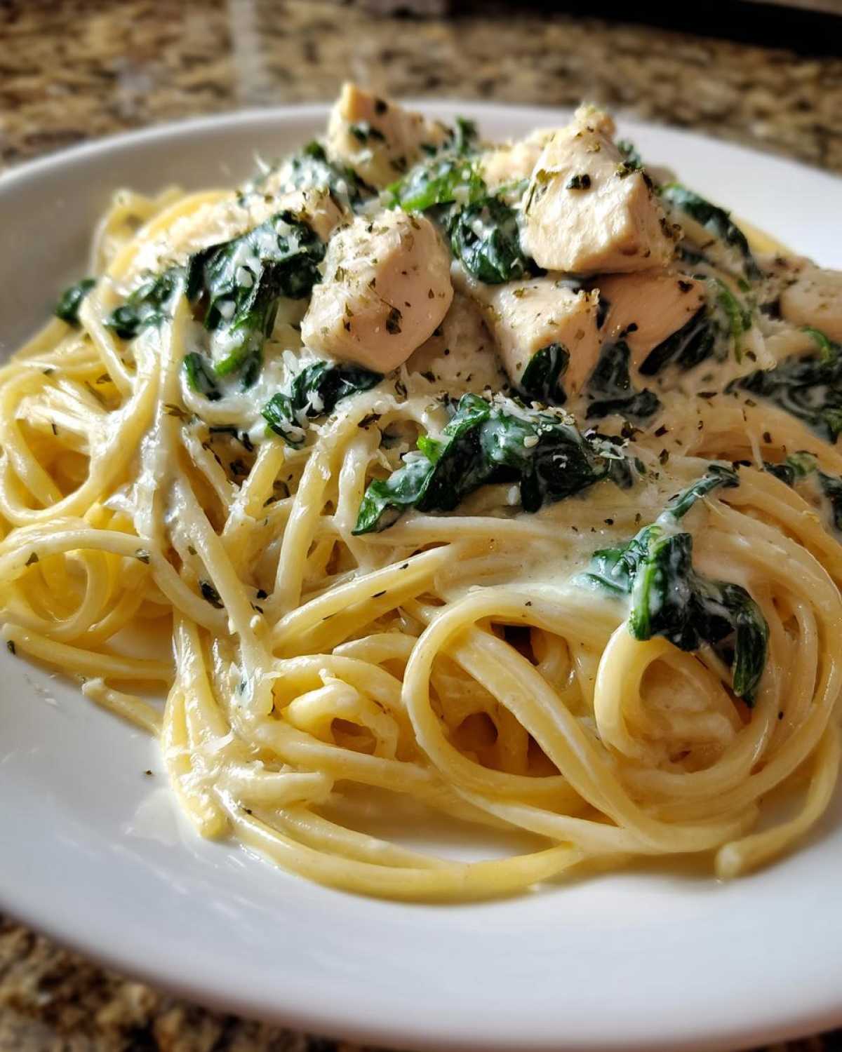 Close-up of a serving of Creamy Spinach Chicken Pasta with Alfredo Sauce, featuring spaghetti, diced chicken, and wilted spinach.