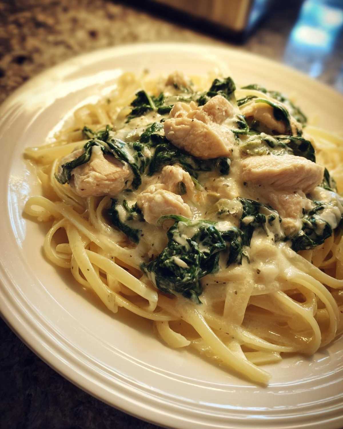 Close-up of a serving of Creamy Spinach Chicken Pasta with Alfredo Sauce featuring fettuccine, chunks of chicken, and wilted spinach.