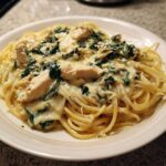 A close-up serving of Creamy Spinach Chicken Pasta with Alfredo Sauce, featuring spaghetti, chunks of chicken, and wilted spinach.