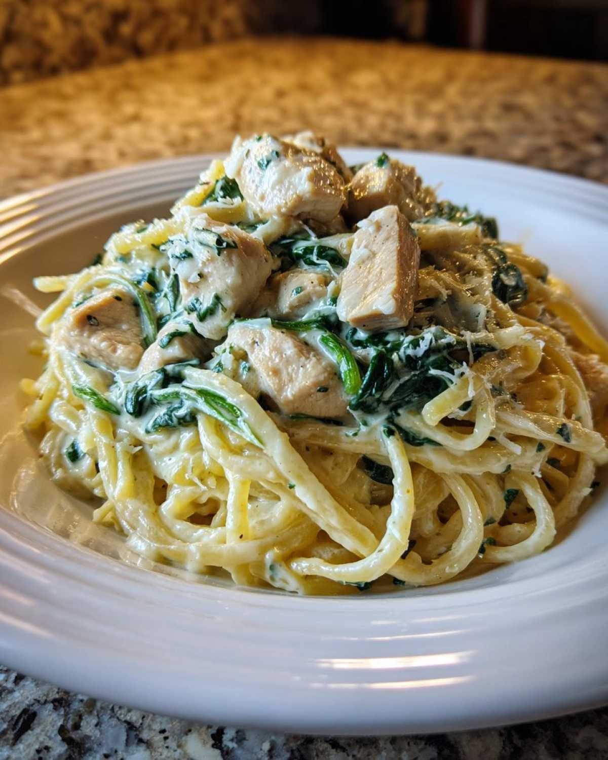 A close-up of a serving of Creamy Spinach Chicken Pasta with Alfredo Sauce, topped with diced chicken breast.