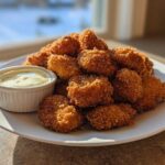 A plate piled high with golden brown Crispy Chicken Nuggets next to a small ramekin of creamy garlic dip.