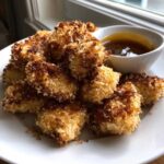 A plate piled high with golden, crispy chicken nuggets drizzled with sauce, served with a side of honey garlic dip.