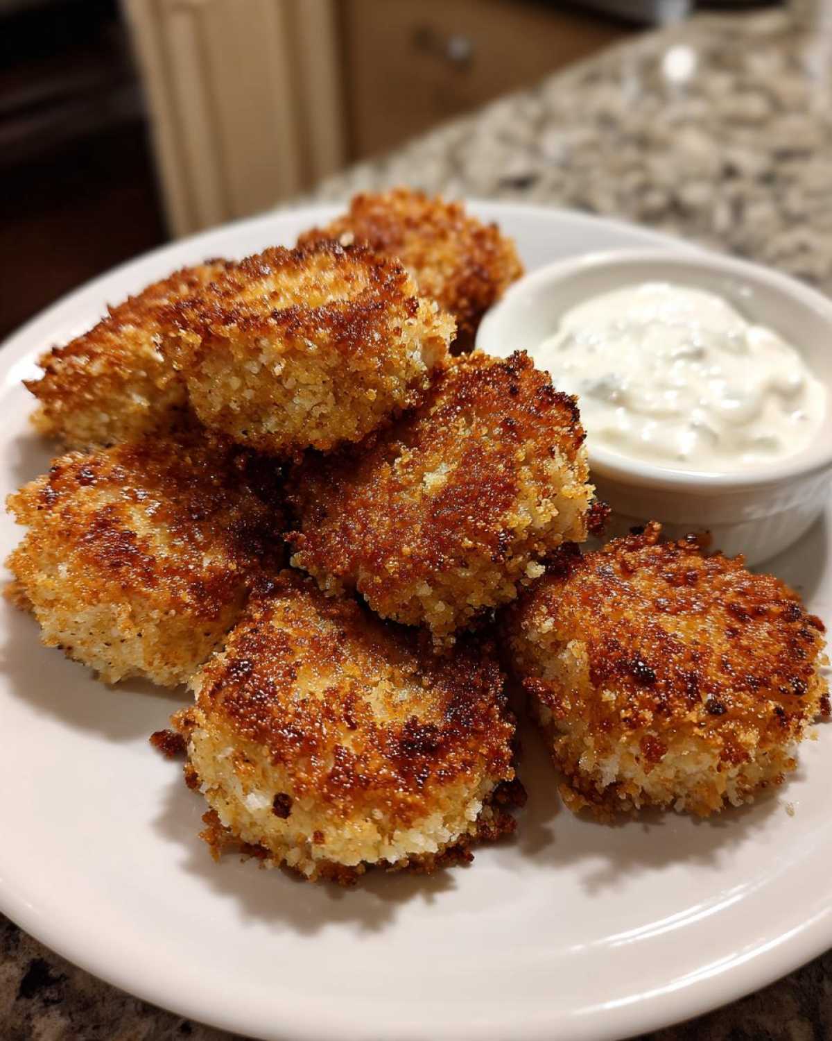A plate of golden brown, crispy chicken nuggets served with a side of creamy ranch dip.