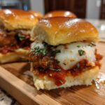 A close-up of one of the Crispy Chicken Parmesan Sliders with melted mozzarella cheese and parsley on a wooden board.