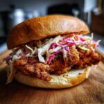 A close-up of a delicious Crispy Chicken Sandwich with Creamy Slaw piled high on a brioche bun.