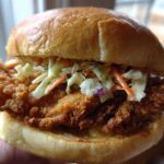 A close-up shot of a perfectly assembled Crispy Chicken Sandwich with Creamy Slaw on a toasted brioche bun.