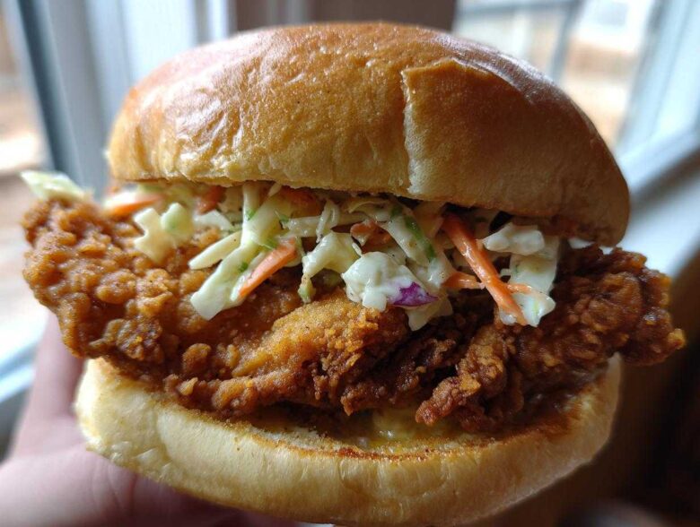 A close-up shot of a perfectly assembled Crispy Chicken Sandwich with Creamy Slaw on a toasted brioche bun.