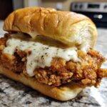 Close-up of a Crispy Chicken Sandwich with Garlic Parmesan Sauce dripping over the fried chicken patty on a toasted bun.