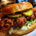 A close-up of a juicy Crispy Chicken Sandwich with Spicy Honey Sauce, topped with pickles and served on a brioche bun.