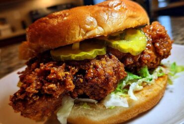 A close-up of a juicy Crispy Chicken Sandwich with Spicy Honey Sauce, topped with pickles and served on a brioche bun.