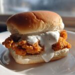 A single, delicious Crispy Chicken Slider generously topped with creamy garlic sauce, served on a white plate.