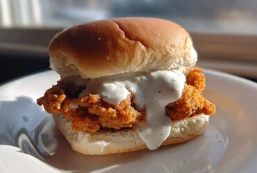A single, delicious Crispy Chicken Slider generously topped with creamy garlic sauce, served on a white plate.