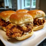 Four homemade Crispy Chicken Sliders with honey mustard sauce drizzled over the fried chicken on soft brioche buns.