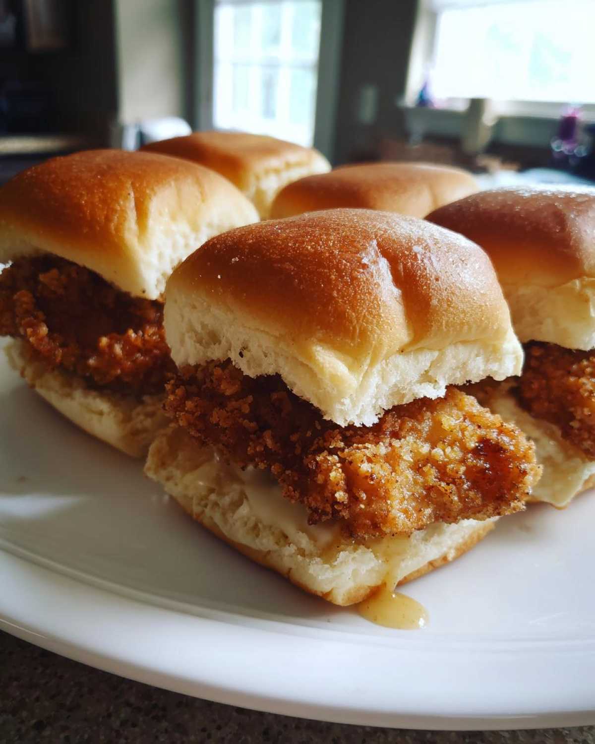 A close-up of several Crispy Chicken Sliders with Honey Mustard on a white plate, showing the golden fried chicken and dripping sauce.