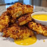 A pile of golden brown Crispy Chicken Tenders served with a side of bright yellow honey mustard sauce.
