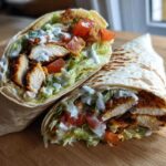 Two halves of a Crispy Chicken Wrap with Creamy Ranch Sauce, showing seasoned chicken, lettuce, and tomatoes inside a toasted tortilla.