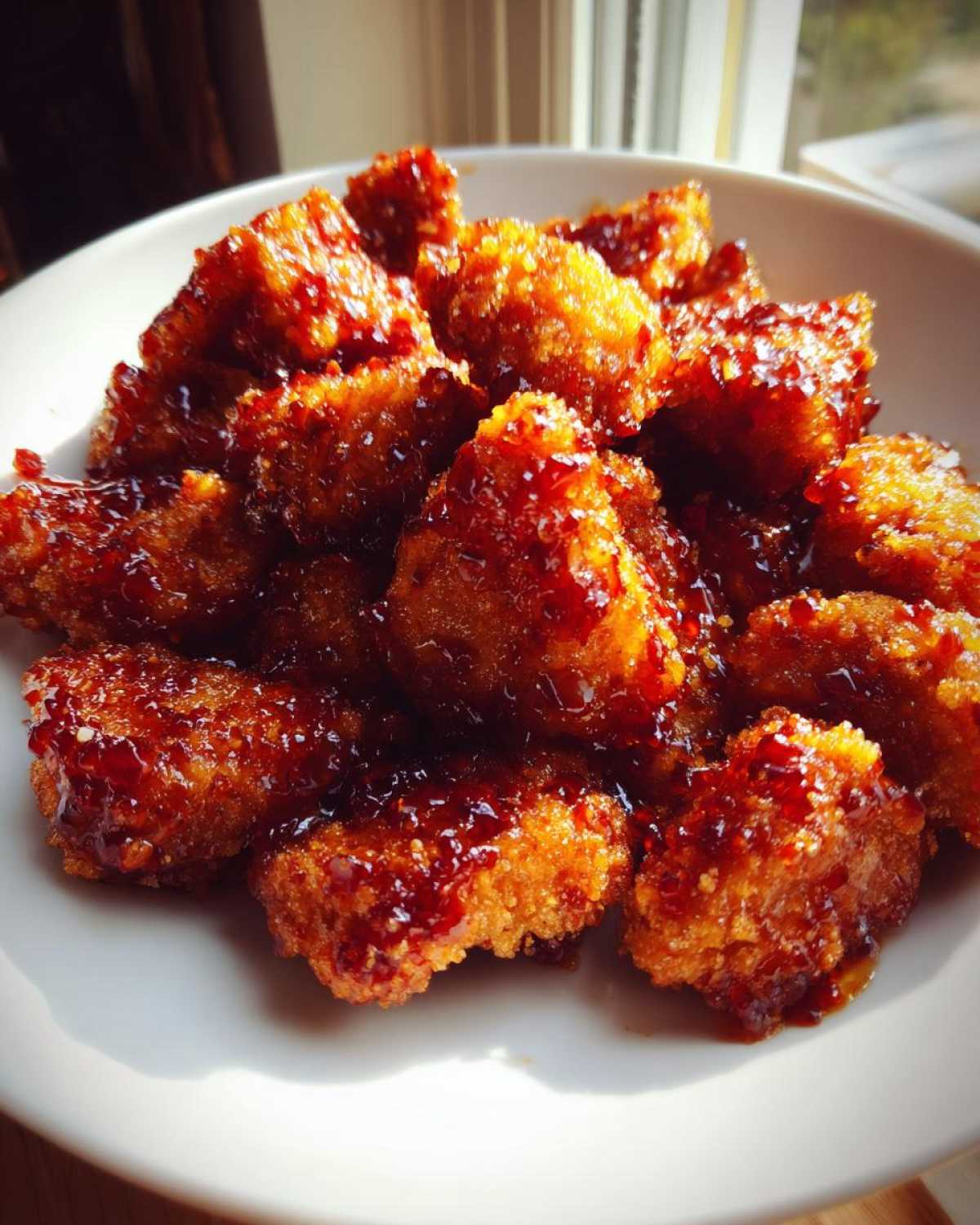 A close-up of golden Crispy Honey Butter Chicken Bites coated in a shiny, dark glaze, served in a white bowl.