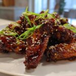 Close-up of crispy oven baked Sticky Teriyaki Chicken Wings coated in dark glaze, topped with sesame seeds and green onions.