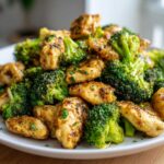 A close-up shot of tender pieces of Garlic Butter Chicken and broccoli florets mixed together on a white plate.