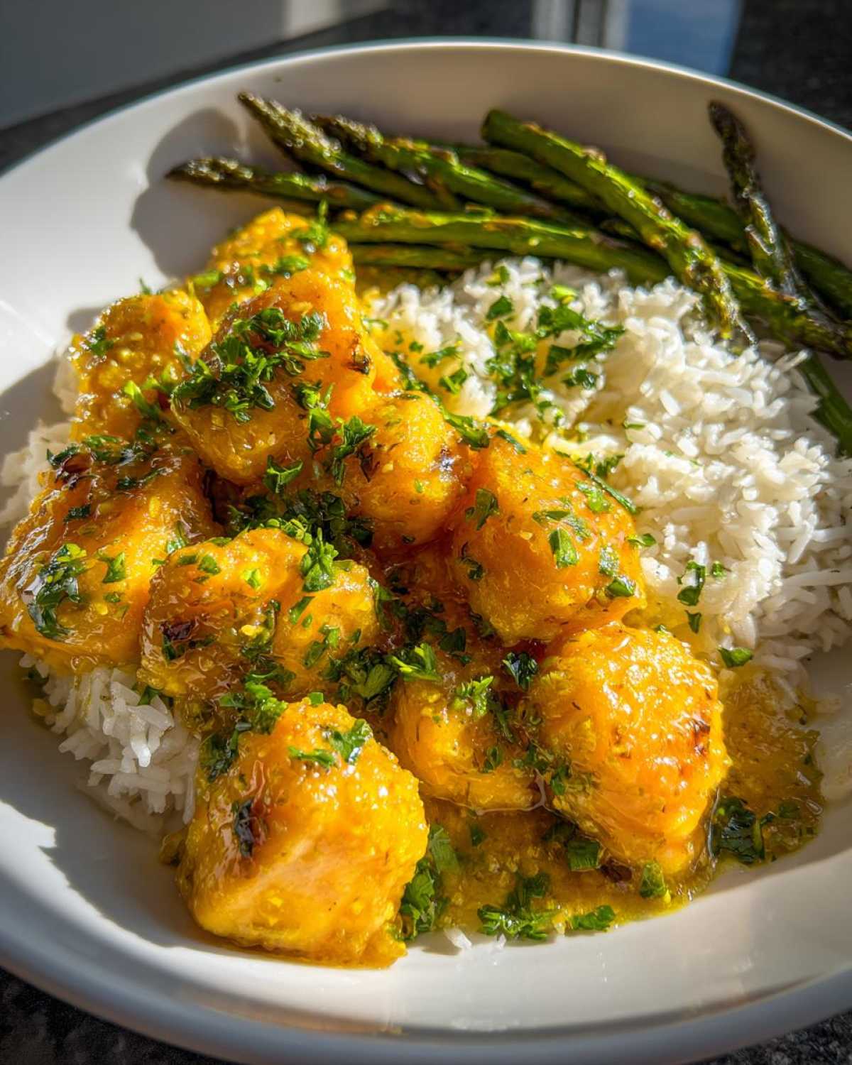 Close-up of Garlic Butter Salmon Bites served over white rice with roasted asparagus and fresh parsley.