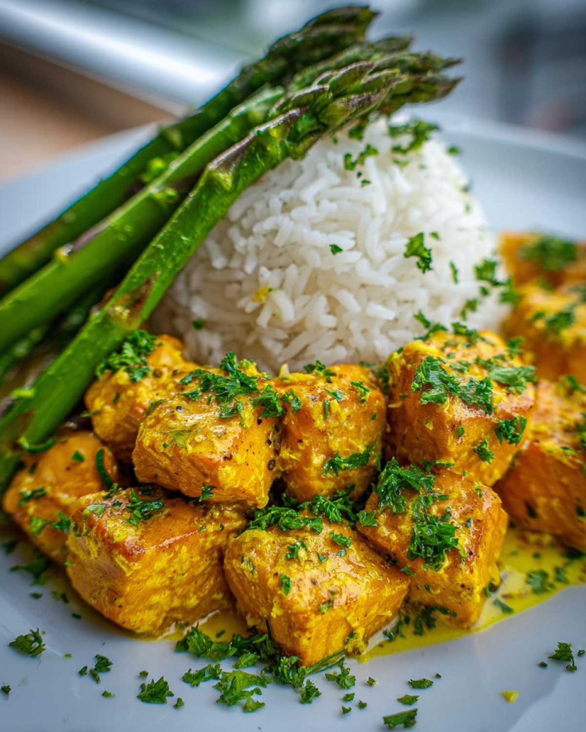 Close-up of Garlic Butter Salmon Bites coated in a yellow sauce, served with white rice and steamed asparagus.