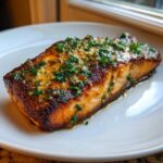 A perfectly cooked fillet of Garlic Butter Salmon with crispy edges, topped with melted butter sauce and fresh parsley.