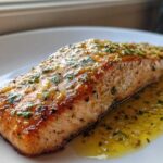 A close-up of a perfectly cooked fillet of Garlic Butter Salmon with Lemon Garlic Sauce drizzled over it.