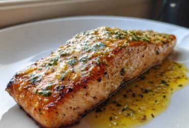 A close-up of a perfectly cooked fillet of Garlic Butter Salmon with Lemon Garlic Sauce drizzled over it.