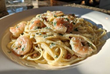 Close-up of a white bowl filled with Garlic Butter Shrimp Pasta with Cream Sauce, topped with parsley.