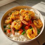 A close-up bowl of Garlic Butter Shrimp with Rice and Veggies, featuring bright yellow shrimp over white rice and mixed peas and carrots.