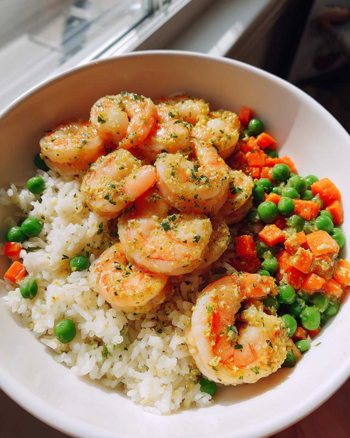 A white bowl filled with Garlic Butter Shrimp with Rice and Veggies, featuring plump shrimp coated in garlic butter over white rice and mixed peas and carrots.