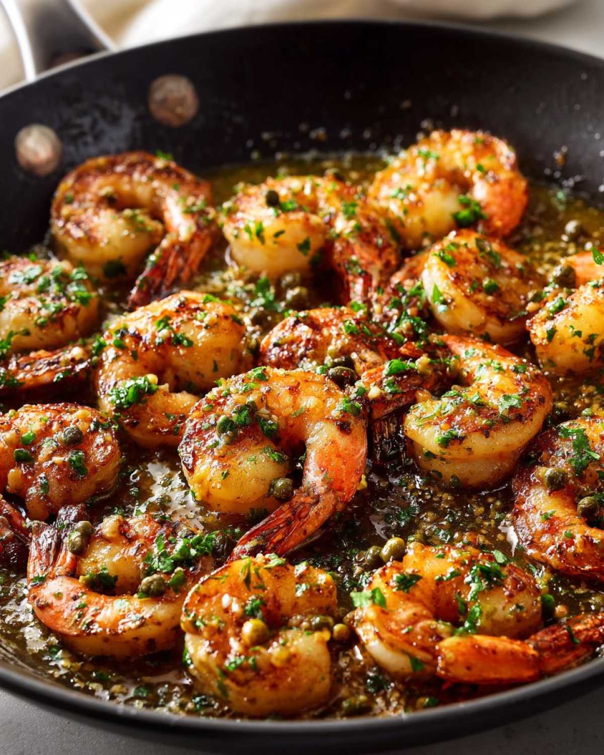 Close-up of plump shrimp sizzling in a skillet with rich garlic butter sauce, capers, and fresh parsley, ready for Garlic Butter Shrimp Skillet.