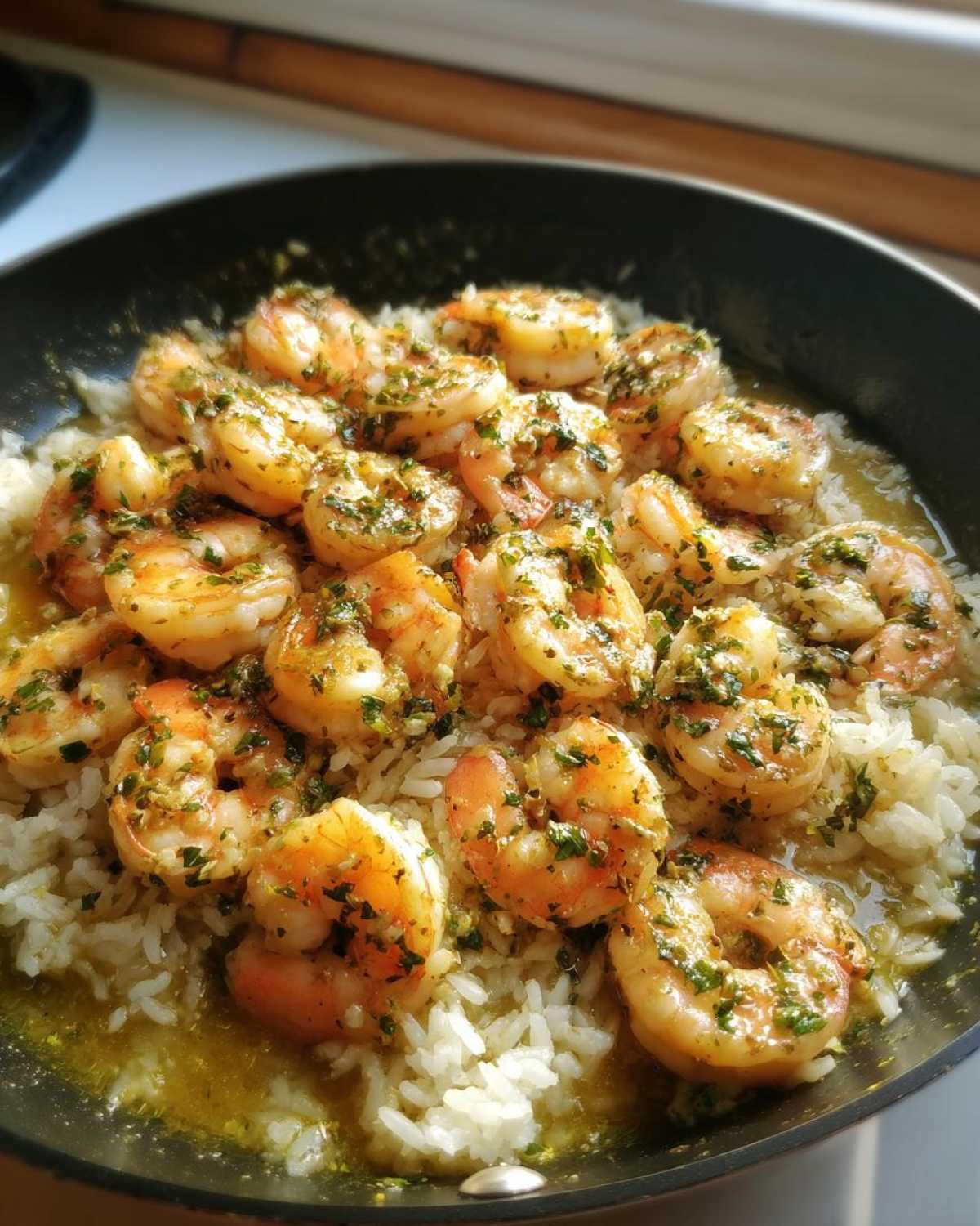 Close-up of juicy shrimp coated in garlic butter and herbs served over white rice in a black skillet.