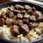 Close-up of tender steak bites coated in garlic butter sauce served over white rice in a black skillet, perfect Garlic Butter Steak and Rice Skillet Dinner.