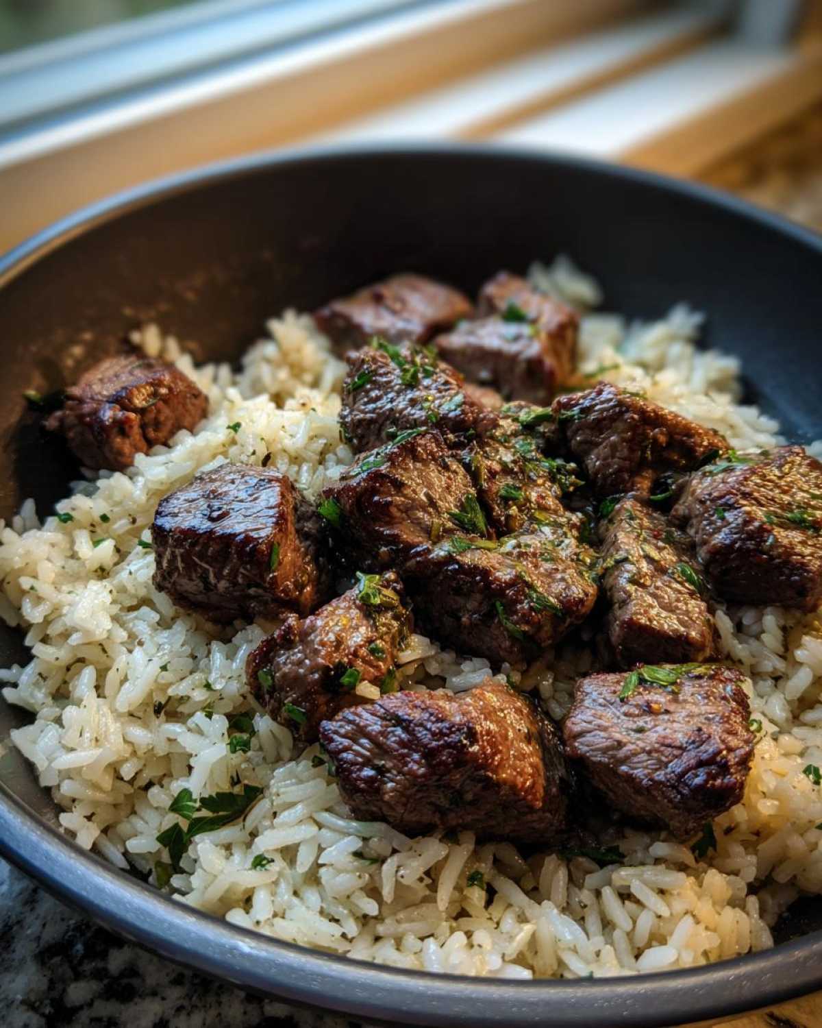 Close-up of juicy steak bites served over white rice in a dark bowl, representing a Garlic Butter Steak and Rice Skillet Dinner.