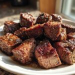 A plate piled high with juicy Garlic Butter Steak Bites featuring crispy, seasoned edges glistening in the light.