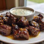 Close-up of seared Garlic Butter Steak Bites glistening in sauce, served with a side of creamy garlic sauce.