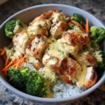 Close-up of a Honey Garlic Chicken Bowl featuring seared chicken pieces, creamy sauce, white rice, broccoli, and shredded carrots.