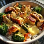 Close-up of a Honey Garlic Chicken Bowl with rice, bright green broccoli, and drizzled with a creamy yellow sauce.
