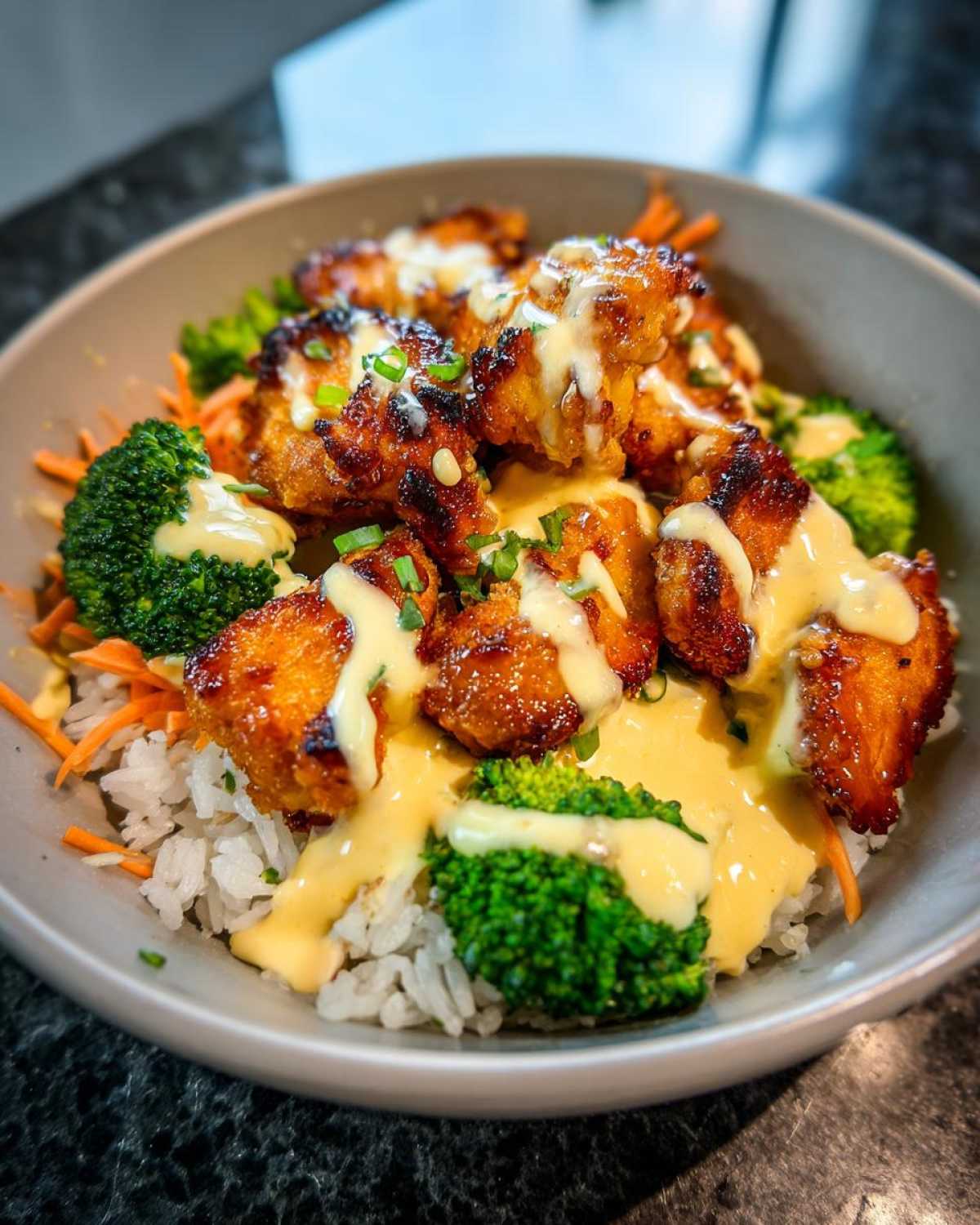 Close-up of a Honey Garlic Chicken Bowl featuring glazed chicken pieces, white rice, broccoli, and a generous drizzle of creamy sauce.