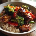 Close-up of a Honey Garlic Chicken Bowl with brown rice, broccoli, and red peppers coated in a shiny sauce.