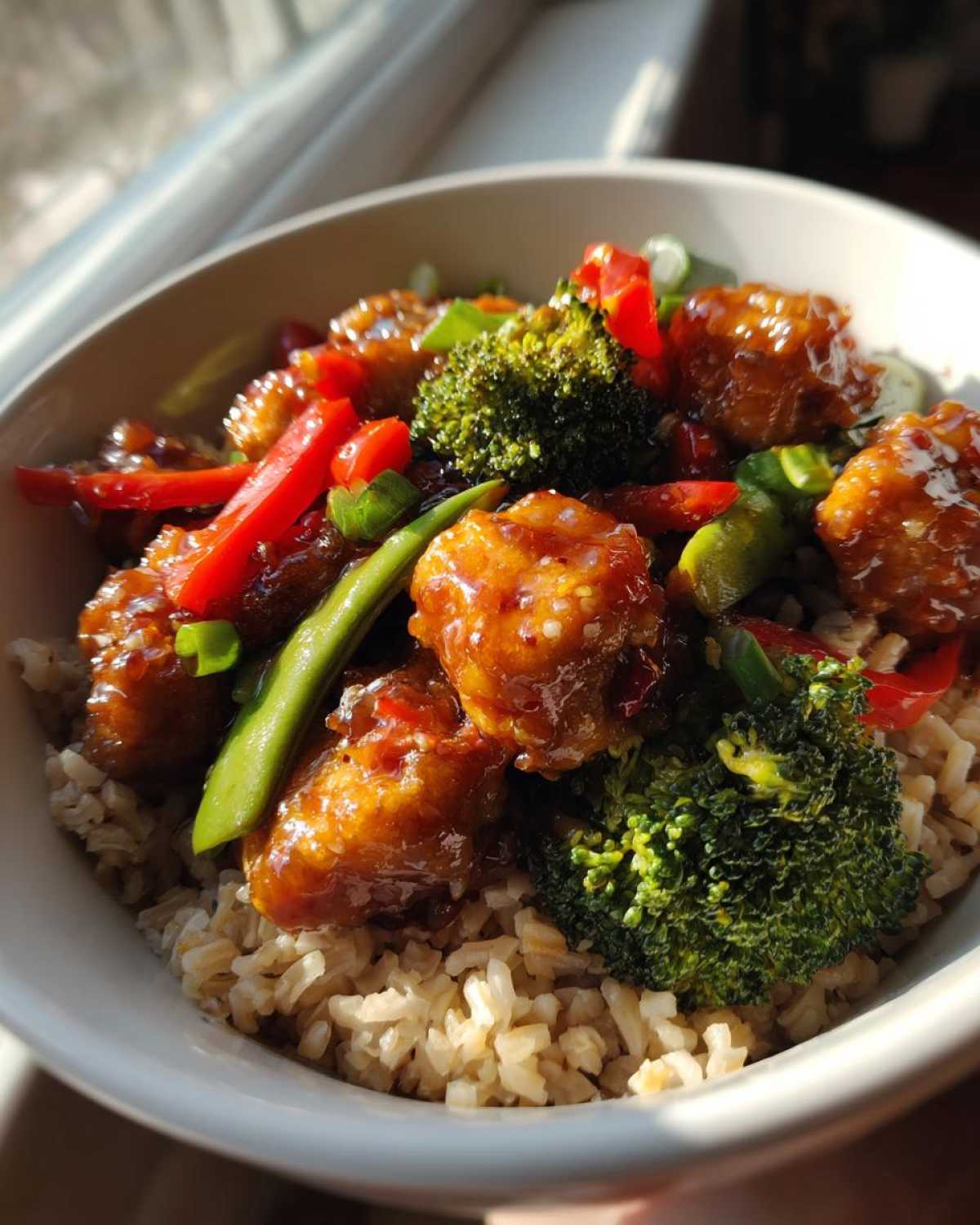 Close-up of a Honey Garlic Chicken Bowl with brown rice, broccoli, red peppers, and snap peas.