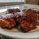 Four pieces of glossy, caramelized Honey Garlic Chicken Thighs with crispy skin served on a white plate.