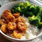 A close-up of a Honey Garlic Shrimp Bowl Quick Dinner featuring glazed shrimp, white rice, and steamed broccoli florets, sprinkled with sesame seeds.