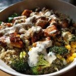 Close-up of a Honey Mustard Chicken Bowl featuring glazed chicken pieces, quinoa, roasted broccoli, corn, and drizzled with creamy sauce.