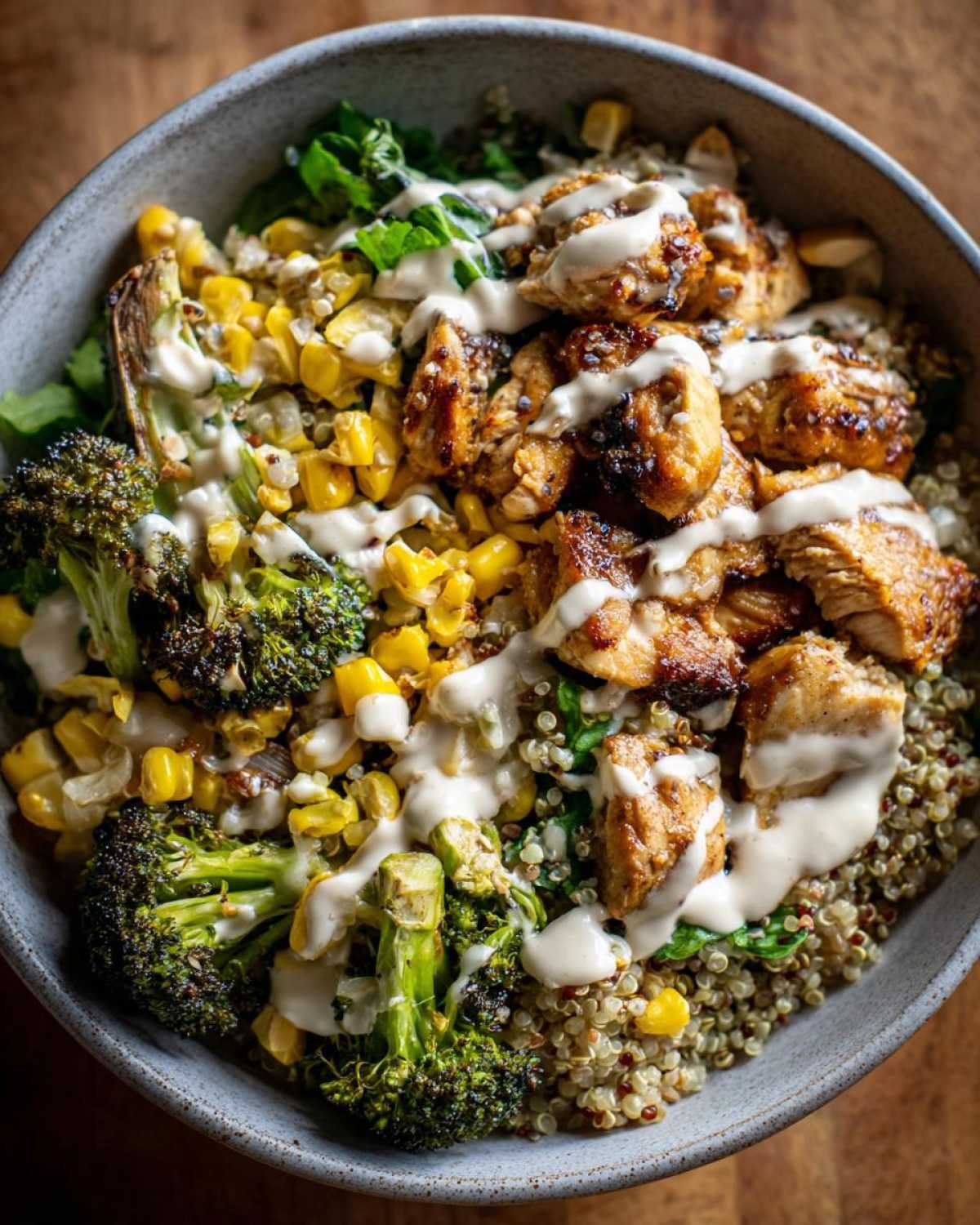 Close-up of a Honey Mustard Chicken Bowl featuring seared chicken, roasted broccoli, corn, and quinoa drizzled with creamy sauce.
