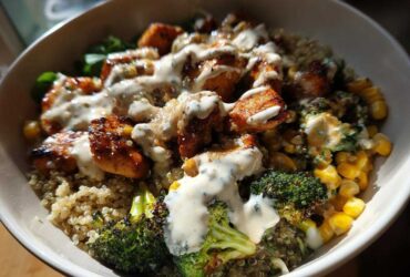 Close-up of a Honey Mustard Chicken Bowl featuring glazed chicken pieces, quinoa, roasted broccoli, corn, and drizzled with creamy sauce.