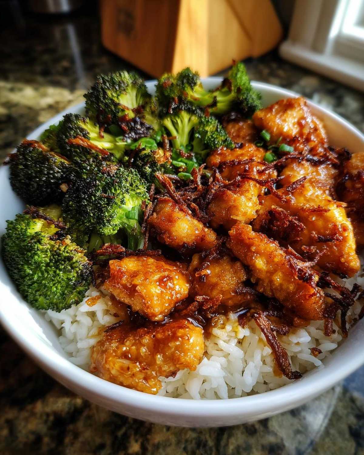 Close-up of a Honey Mustard Chicken Bowl with rice, glazed chicken pieces, roasted broccoli, and crispy fried onions.